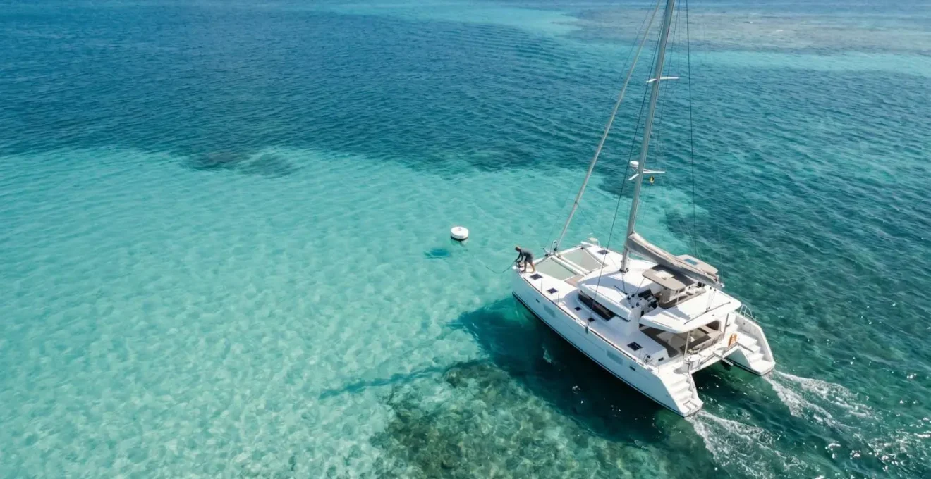 Vue aérienne d'un catamaran effectuant une manœuvre d'approche vers une bouée d'amarrage blanche dans une baie caribéenne
