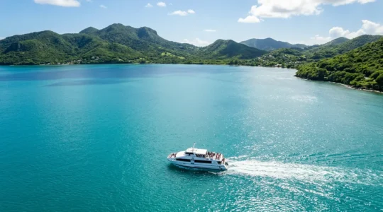 Vue aérienne d'un bateau-bus naviguant sur les eaux turquoise de la rade de Pointe-à-Pitre en Guadeloupe, avec la silhouette des îles en arrière-plan